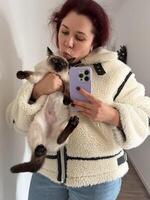 Cozy moment captured as woman holds a Siamese cat and takes a mirror selfie. Dressed in a fluffy jacket and holding smartphone, warm and intimate scene is framed by the hallway background photo
