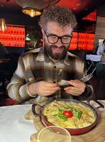Millennial man enjoying a delicious meal in a stylish restaurant setting. Vibrant red backdrop and beautifully plated dish create a warm and inviting dining atmosphere photo