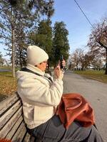 Woman taking a photo in a park on a sunny autumn day, moments of leisure and connection with nature amidst fall cold scenery