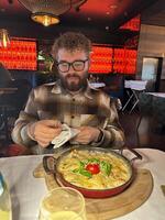 Millennial man enjoying a delicious meal in a stylish restaurant setting. Vibrant red backdrop and beautifully plated dish create a warm and inviting dining atmosphere photo