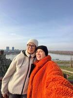 Joyful couple mother and daughter takes a selfie against a scenic river backdrop in autumn, warm outfits and happy expressions. Social networks and blogger concept photo