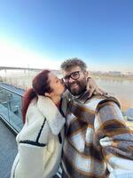 Man and woman taking selfie in cold time outdoor. Couple enjoying a beautiful day by the river with a breathtaking view. Moment of connection and joy together photo
