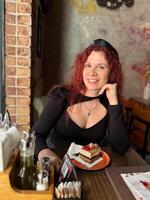 Millennial woman with red hair sits thoughtfully at a rustic cafe table, surrounded by a cozy and artistic atmosphere. Soft lighting and her pensive expression convey photo