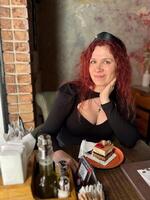 Millennial woman with red hair sits thoughtfully at a rustic cafe table, surrounded by a cozy and artistic atmosphere. Soft lighting and her pensive expression photo