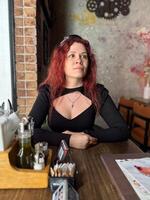 Millennial woman with red hair sits thoughtfully at a rustic cafe table, surrounded by a cozy and artistic atmosphere. Soft lighting and her pensive expression photo