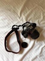 Camera with a strap placed on a white bed sheet, capturing the essence of travel preparation and creativity. Simplicity, creative and readiness of a photographer journey. Top view photo