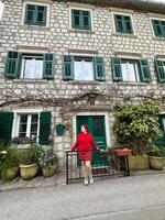 Charming stone building with green shutters and millennial woman in red standing in front. a picturesque scene capturing the essence of rustic architecture and fashion. Travel and journey concept photo