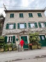 Charming stone building with green shutters and millennial woman in red standing in front. a picturesque scene capturing the essence of rustic architecture and fashion. Travel and journey concept photo