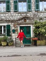 Charming stone building with green shutters and millennial woman in red standing in front. a picturesque scene capturing the essence of rustic architecture and fashion. Travel and journey concept photo