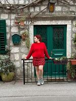 Charming stone building with green shutters and millennial woman in red standing in front. a picturesque scene capturing the essence of rustic architecture and fashion. Travel and journey concept photo