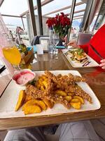 delicious meal is served on a glass table with a scenic view in the background, featuring crispy battered food and vibrant garnishes. a bright orange drink complements the setting photo