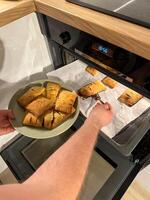 Freshly baked pastries are being taken out of the oven, steaming and golden brown, ready to be served on a green plate. Aroma of crispy dough fills the cozy kitchen photo