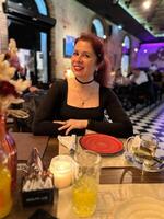 Millennial woman enjoying a pleasant evening at a lively restaurant, seated at a table with a red plate and warm candlelight. Atmosphere is night with a mix of modern and cozy interior design, photo