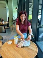 Woman with long red hair enjoys a casual moment at a coffee shop. Girl drink coffee in cafe. Bright interior and large windows create a cozy and inviting atmosphere. Breakfast time photo