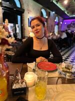 Millennial woman enjoying a pleasant evening at a lively restaurant, seated at a table with a red plate and warm candlelight. Atmosphere is night with a mix of modern and cozy interior design photo