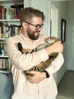 Handsome millennial man holds a tabby cat in his arms and kisses it. Pet and friendship concept photo