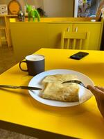Breakfast setting with a plate of crepes and a frothy cappuccino on a bright yellow table. Cafe with modern design. Pancakes with different fillings. Food concept photo