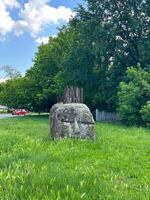 Large stone sculpture resembling a face is situated in a grassy area, with rusted metal spikes protruding from its top photo