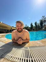 Millennial man taking selfie by swimming pool. Vibrant blue water and relaxed setting create a perfect atmosphere for summer fun. Holidays and vacation photo