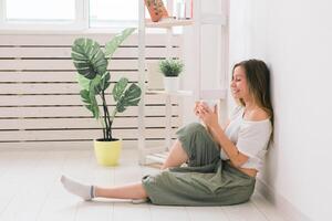 Dreaming girl sitting on floor at home and drink tea from cup photo