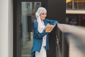 Smiling muslim girl using digital tablet, browsing Internet or social networks outdoor, copy space photo