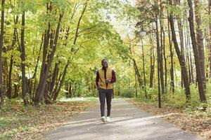 Cheerful african american young man in stylish clothes walks in autumn park on sunny warm autumn day. Concept of weekend and outdoor recreation photo