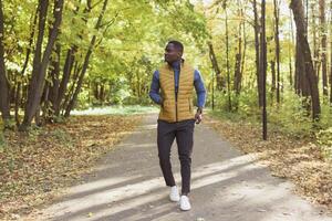 Cheerful african american young man in stylish clothes walks in autumn park on sunny warm autumn day. Concept of weekend and outdoor recreation photo