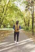 Cheerful african american young man in stylish clothes walks in autumn park on sunny warm autumn day. Concept of weekend and outdoor recreation photo