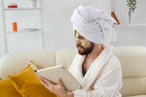 Bearded man enjoys with a cosmetic mask on his face made from slices of cucumber. Men skin care and spa at home concept photo