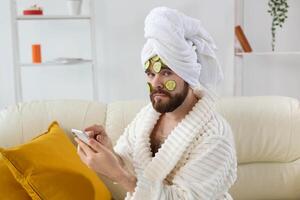 Bearded man enjoys with a cosmetic mask on his face made from slices of cucumber. Men skin care and spa at home concept photo