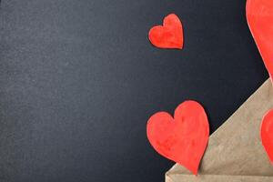 Red hearts drop out of crafting brown envelope on black background with a copy of the space photo
