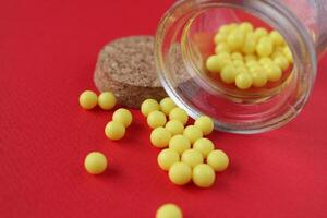 Vitamins homeopathy tablets are sucked out of the packaging jar on a red background with a copyspace close-up photo