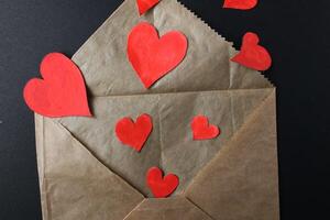 Red hearts drop out of crafting brown envelope on black background with a copy of the space photo