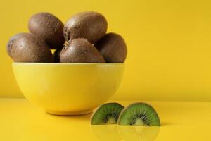 Still life fruit in a yellow bowl plate on a yellow background next to lies a piece of kiwi illuminatiited yellow trend color copyspace photo