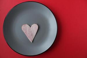 Still life breakfast for Valentine's Day Heart of ham sausage on a gray plate on a red bright background with a copy of the space photo