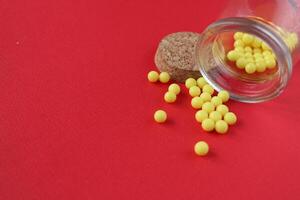 Vitamins homeopathy tablets are sucked out of the packaging jar on a red background with a copyspace close-up photo