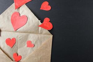 Red hearts drop out of crafting brown envelope on black background with a copy of the space photo