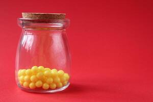 vitamins homeopathy in a glass test tube jar yellow little balls on a red bright background with a place to text copyspace photo