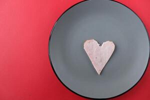 Still life breakfast for Valentine's Day Heart of ham sausage on a gray plate on a red bright background with a copy of the space photo