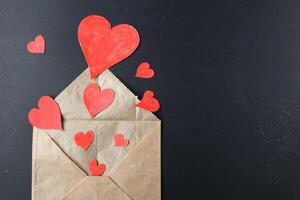Red hearts drop out of crafting brown envelope on black background with a copy of the space photo