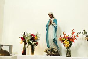 Statue of the Virgin Mary with flowers in a church on a white wall background. Religious symbols photo
