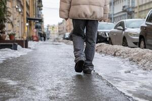 Person walking on slippery sidewalk rear view. Pavement covered with slippery ice. Frozen rain. photo