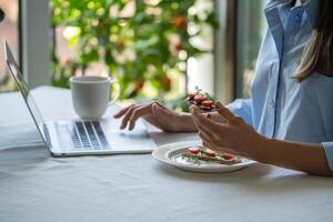 Female has rye crispbread sandwich at table, brows online, work on laptop while eating, snack on go photo