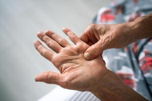 Unseen old woman rubs, feels tender hand with stiff knot under ring finger. Dupuytren contracture photo