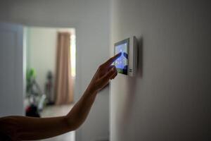 Closeup hand using smart home panel, touching screen with connected appliances device on wall. photo