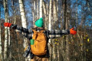 Rearview of free, happy woman with backpack spinning with arms outstretched in autumn forest photo