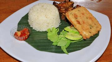 Grilled chicken rice and fried tempeh served on a plate photo