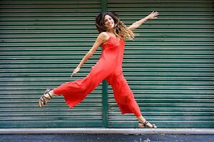 A Joyful Woman in a Red Jumpsuit Dances Playfully Against a Lively Green Background photo