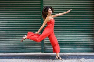 A Joyful Woman Dressed in a Bright Red Jumpsuit is Dancing Joyfully Against a Green Background photo