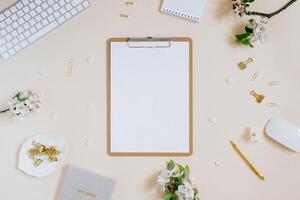 Blogger workplace with glider, white apple flowers, gold stationery, computer, tablet with white blank note paper and pen on beige background with copy space. Flat lay female office desk. photo